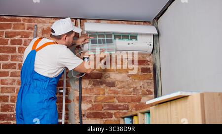 Technician installing air conditioner on brick wall with ladder and tools Stock Photo