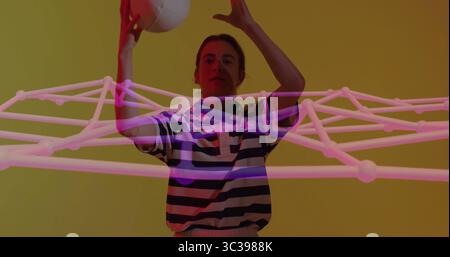 Reaching upward adult woman holding white ball overhead in studio, with pink wireframe network Stock Photo