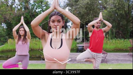 Practicing tree pose woman wearing sports bra guiding yoga on grassy lawn beside pond, with chairs Stock Photo