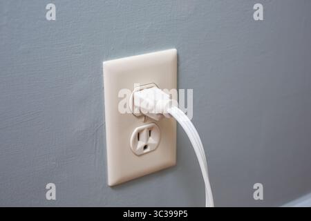 A view of a white electrical cord plugged into a wall socket. Stock Photo