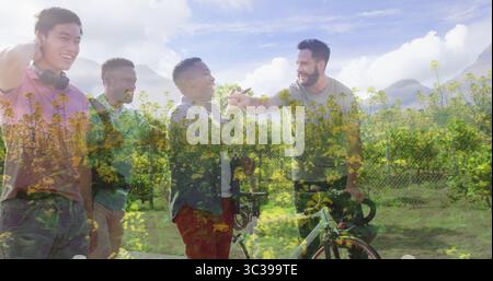 High-fiving four friends wearing headphones, holding bicycles in yellow flower field on gravel path Stock Photo