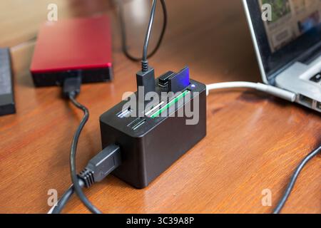 A view of a card reader and port hub connected to a laptop computer, featuring external hard drives, storage cards and cables. Stock Photo