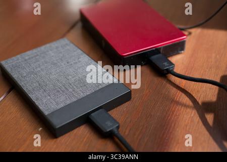 A closeup view of two external hard drives on a wooden table, connected to a computer with a cable. Stock Photo