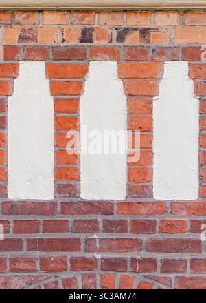 Frontal close-up of three white plaster inlays in a red brick facade, framed by layers of differently toned bricks above and below. Stock Photo