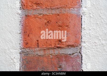 Extreme close-up of a red brick segment framed by white plaster. The image highlights the raw texture, surface imperfections. Stock Photo