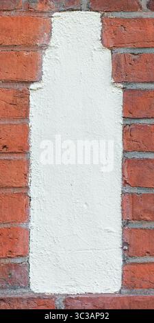 Vertical close-up of a single plastered shape embedded in a red brick wall. Stock Photo