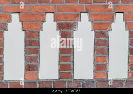 A close-up of a decorative brick wall featuring an alternating pattern of red bricks and white plaster columns. Stock Photo