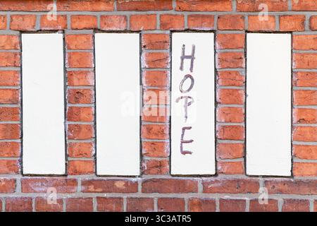 The word “HOPE” is hand-painted in vertical orientation on a cream-colored section of a brick wall. Stock Photo