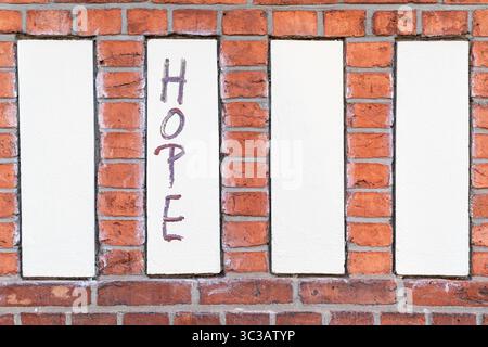 A red brick wall with four vertical white plaster panels. The second panel from the left features the handwritten word “HOPE” in muted purple tones. Stock Photo