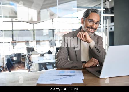 Portrait of happy middle aged business man looking at camera at work desk. Stock Photo