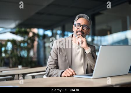 Happy mature business man entrepreneur using laptop outside office looking away. Stock Photo