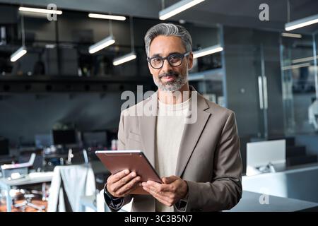 Happy mature business man standing in office using tablet, portrait Stock Photo