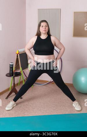 Full length view of adult fitness woman doing physical exercises during morning exercises during fitness training at home in home interior. Woman is d Stock Photo