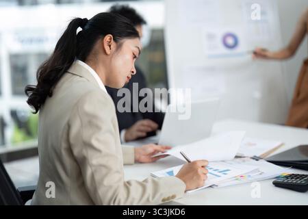Focused Businesswoman Analyzing Reports. Professional woman reviewing data and charts in a modern office. Stock Photo