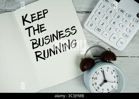 Keep The Business Running text on paper notebook page with alarm clock and calculator on wooden background Stock Photo