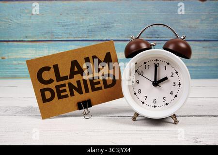 Claim Denied text written on paper card with alarm clock on wooden background Stock Photo