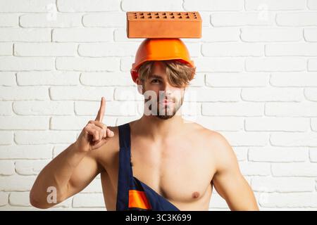 Builder with bricks, funny sale on construction site. Funny builder man with helmet doing brickwork. Builder posing with bricks blocks. Bricklayer Stock Photo