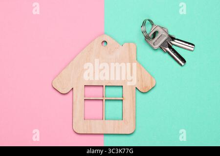 Wooden house figurine or keychain with keys on blue pink background. Top view Stock Photo