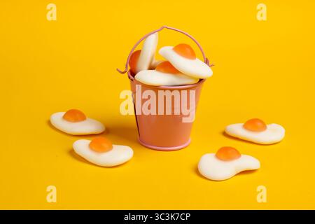 Mini bucket with marmalade fried eggs on yellow background. Sweets, pastel color trend, food concept. Stock Photo
