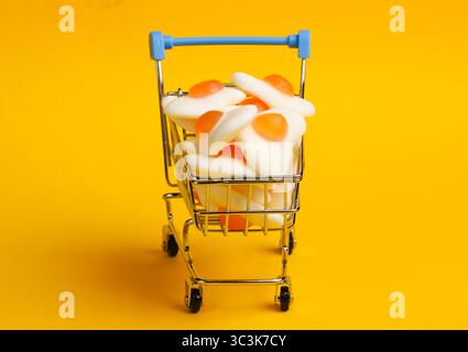 Mini shopping trolley with marmalade fried eggs on a yellow background. Sweets Shopping, Pastel Color Trend, Food Concept Stock Photo