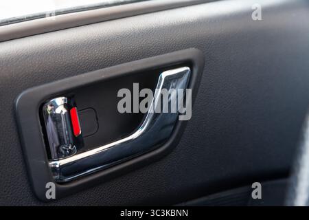 A close-up view of a part of the interior of a modern luxury car with a view of a silver-colored door handle on a chrome finish with black wood trim a Stock Photo