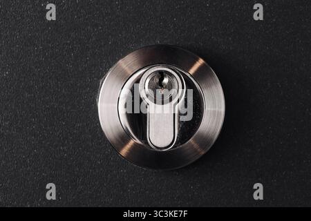 Door lock cylinder closeup. Metallic security system on black background. Safety equipment macro view. Modern round lock with keyhole. Stock Photo