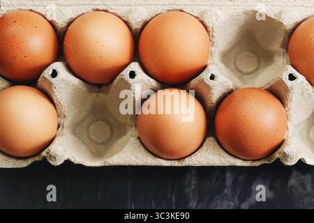 Brown eggs in carton. Organic eggs in recycled paper tray on dark background. Healthy protein food. Farm product closeup. Eco-friendly packaging. Stock Photo