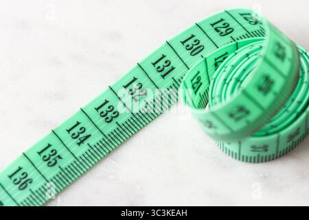 Measuring tape closeup. Green tailor centimeter on white surface. Flexible metric tool for sewing, tailoring and weight loss tracking. Stock Photo