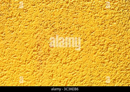 Yellow plaster wall texture. Vibrant painted surface closeup. Rough stucco background with strong color. Bright decorative facade. Stock Photo