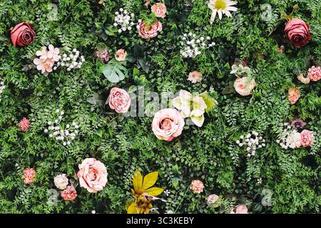 Artificial flower wall background. Colorful roses and leaves. Decorative greenery with plastic blossoms. Event decoration concept. Lush fake plants. Stock Photo