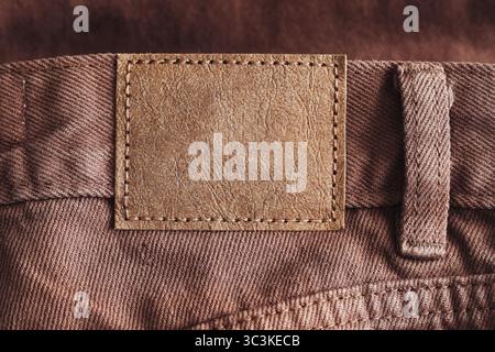 Close up of jeans label. Brown fabric trousers with leather tag. Empty patch for custom branding or text. Macro view of textile texture. Fashion space Stock Photo