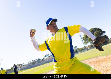 Male baseball player pitching baseball on mound at baseball field in yellow-blue uniform with glove Stock Photo