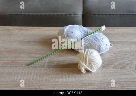 Knitting Supplies with Yarn Balls and a Green Knitting Needle on a Wooden Table Stock Photo
