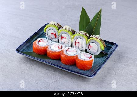Colorful sushi rolls with salmon, avocado, shrimp, cream cheese, and roe, topped with sauce and crunchy bits, served on a blue rectangular plate. Stock Photo