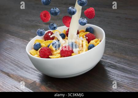 Falling corn flakes with fresh berries and pouring milk on wooden background Stock Photo