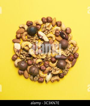 Pattern of nuts mix. Hazelnut, macadamia, almonds, walnut, cashew, brazil nut, on yellow background. Top view. Stock Photo