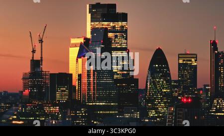 Warm sunset over London iconic skyline, featuring 30 St Mary Axe (The Gherkin), with construction cranes symbolizing growth in the bustling metropolis. Cityscape night background. Drone flight Stock Photo