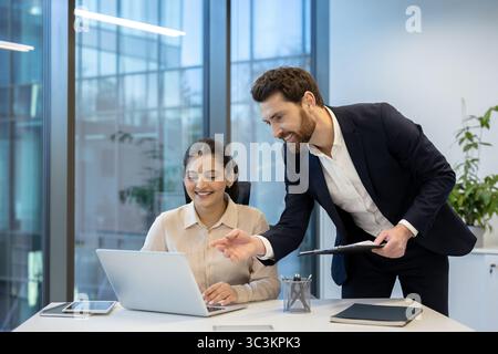 A diverse team collaborates in a modern office, working together on a laptop. Professionalism and teamwork are evident in the scene. Stock Photo