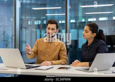 A businessman gestures while explaining something to a businesswoman at a modern office. Stock Photo