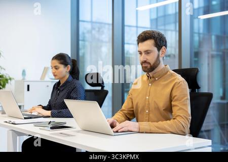 Two professionals work at their computers in a modern office setting, focusing on their tasks with a clean workspace. Stock Photo