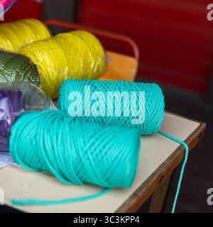 Colorful skeins of yarn and plastic cord in turquoise, yellow, green, purple, and burgundy tones lie on a table. Some are wrapped in packaging, others Stock Photo
