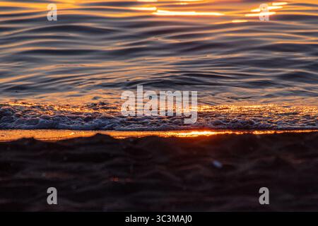 A serene, abstract close-up of a Black Sea sunset. Shimmering golden light reflects on dark, rippling water, creating a tranquil and atmospheric scene Stock Photo