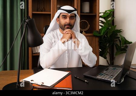 Middle-eastern businessman wearing emirati kandura working in the office - confident emirati businessman wearing traditional kandura working on laptop Stock Photo