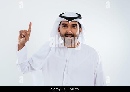 Middle-eastern doctor wearing emirati kandura working in the office - smiling middle eastern businessman in traditional emirati kandura. Pointing upwa Stock Photo