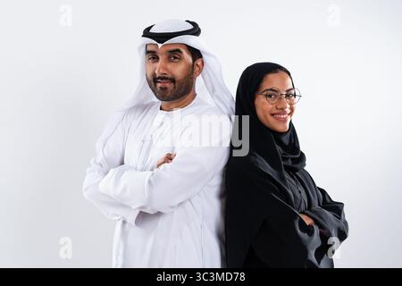 Emirati man and woman are standing back to back in a studio, wearing traditional clothing, with their arms crossed, exuding confidence and cultural pr Stock Photo