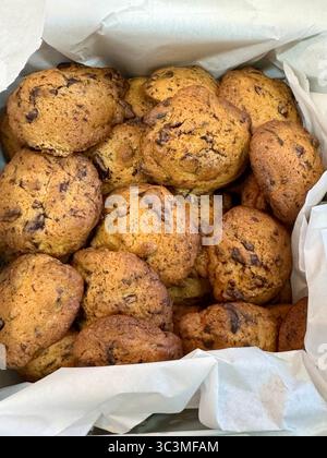 Close-up of freshly homemade baked chocolate chip cookies piled in a box lined with parchment paper. Stock Photo