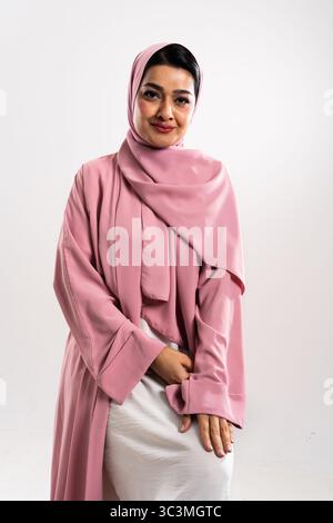 Studio portrait of a confident middle-eastern woman wearing a pink hijab and abaya, showcasing modern islamic fashion and female empowerment Stock Photo