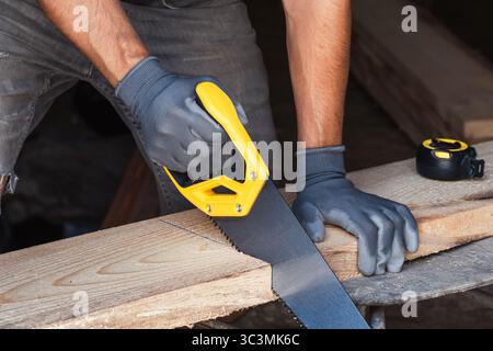 Brutal carpenter saws board with hacksaw in gray gloves Stock Photo