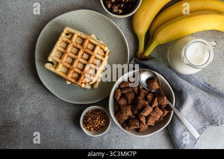 A wholesome breakfast featuring a bowl of chocolate cereals paired with fresh milk, served alongside bananas and waffles on a modern kitchen setting f Stock Photo