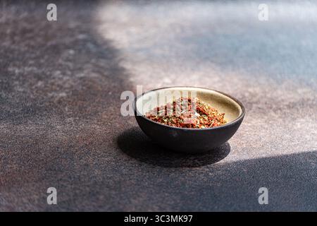 A close-up shot of a vibrant spice blend with tomato, olive, and salt in a dark ceramic bowl. Set against a textured stone background, creating a mini Stock Photo
